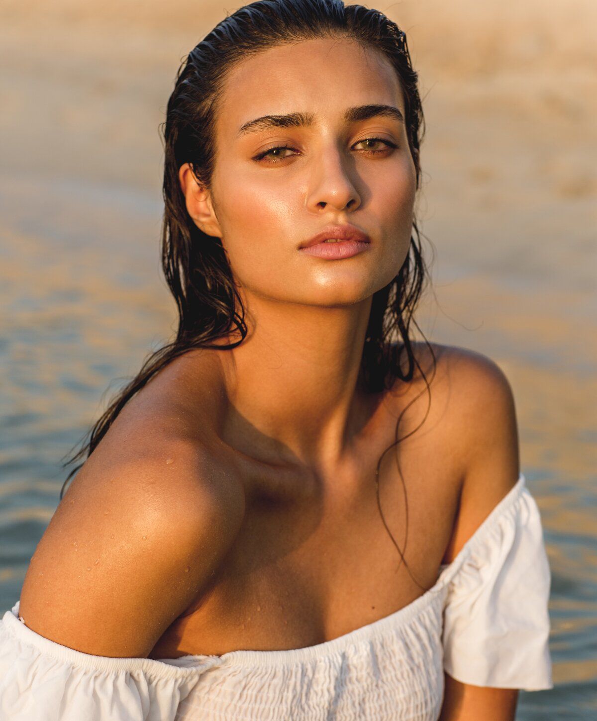 Woman with wet hair against a beach backdrop.